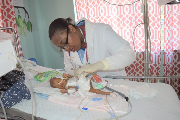 NPH Haití Médico joven con el cabello recogido en un moño que atiende a un bebé prematuro conectado a tubos y vías intravenosas